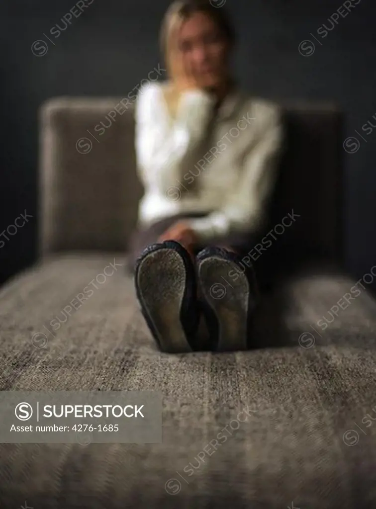 Young woman sitting on divan, holding head, focus on sole of shoes