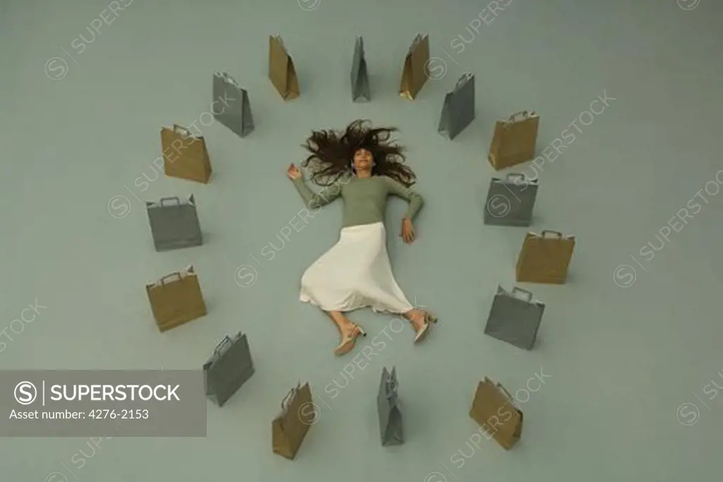 Woman lying on the ground, surrounded by shopping bags, overhead view