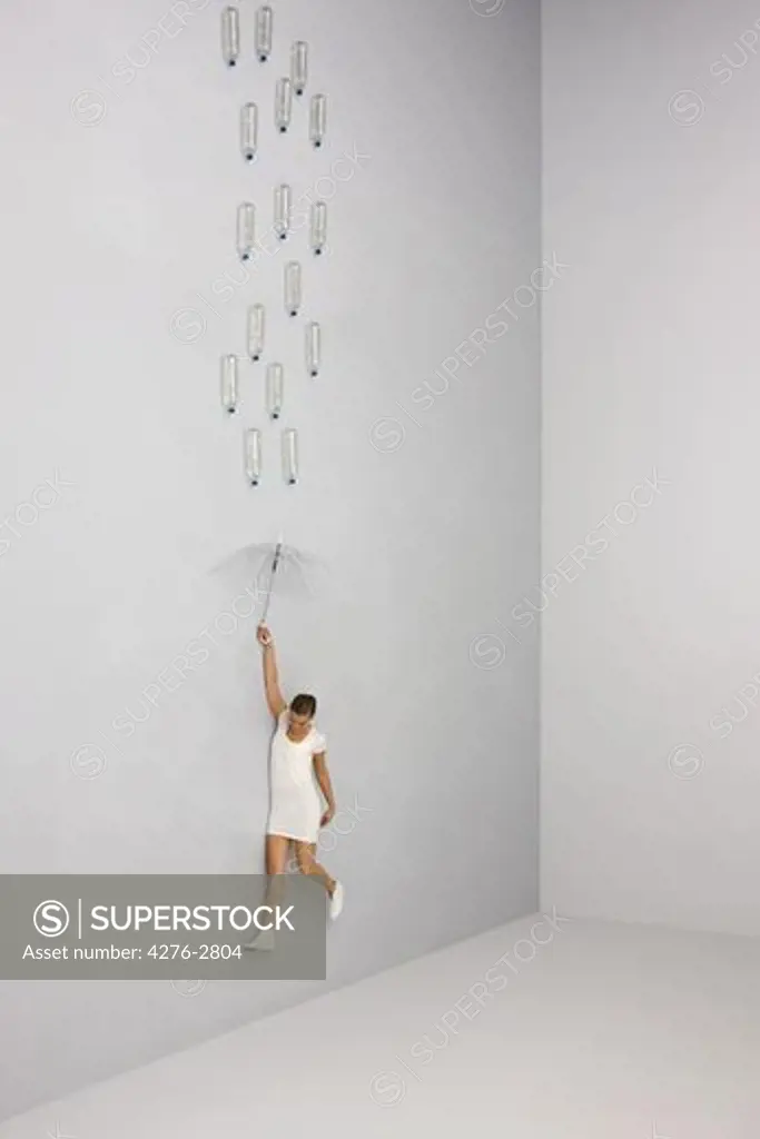 Woman midair holding umbrella beneath raining water bottles