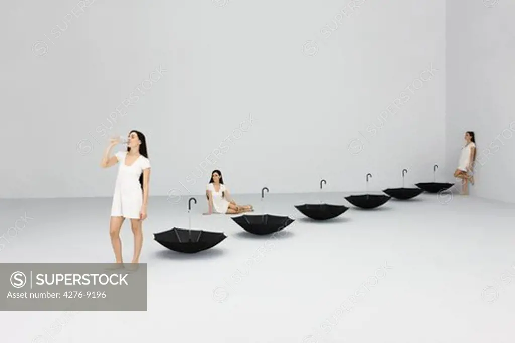 Thirsty woman drinking from bottle, upside down umbrellas lined up nearby, digital composite