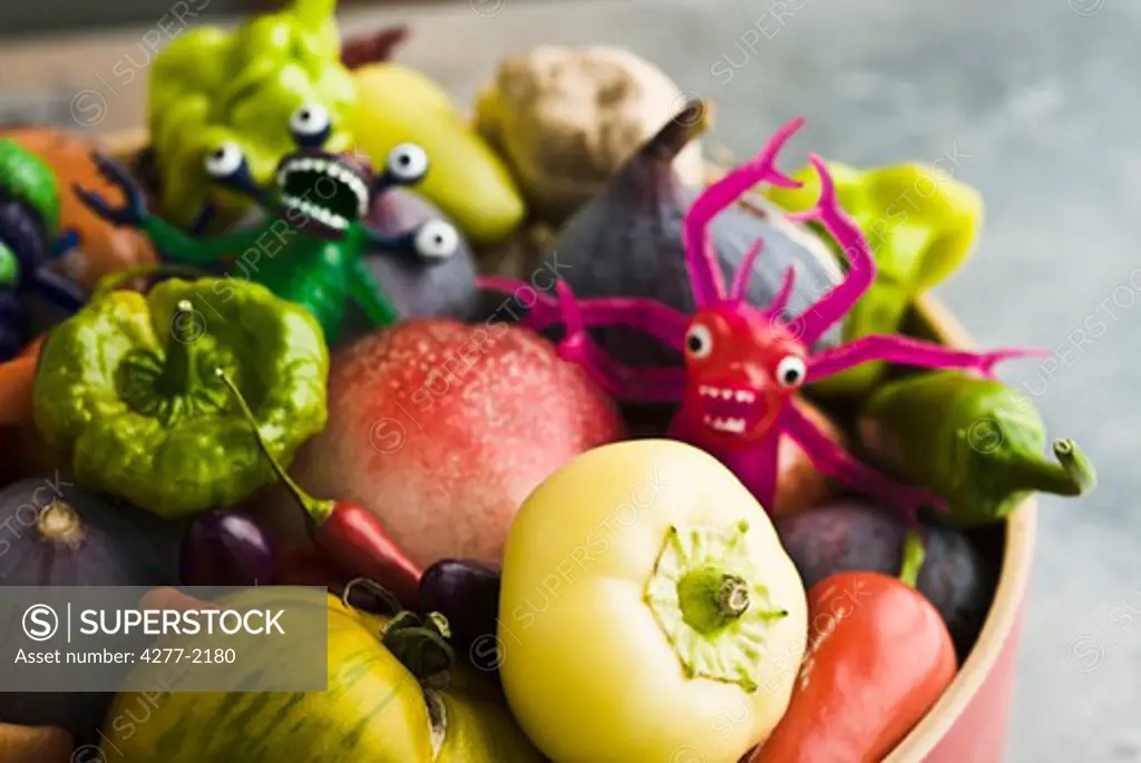 Fresh vegetables and fruit in bowl with plastic monster toys