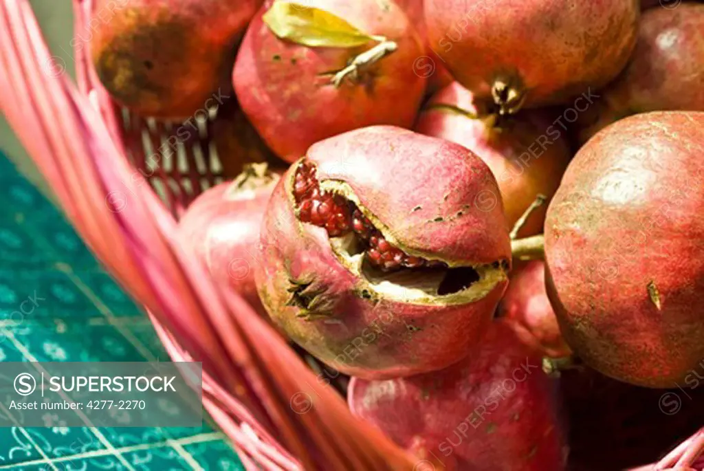 Ripe pomegranates in basket, one cracked open revealing seeds