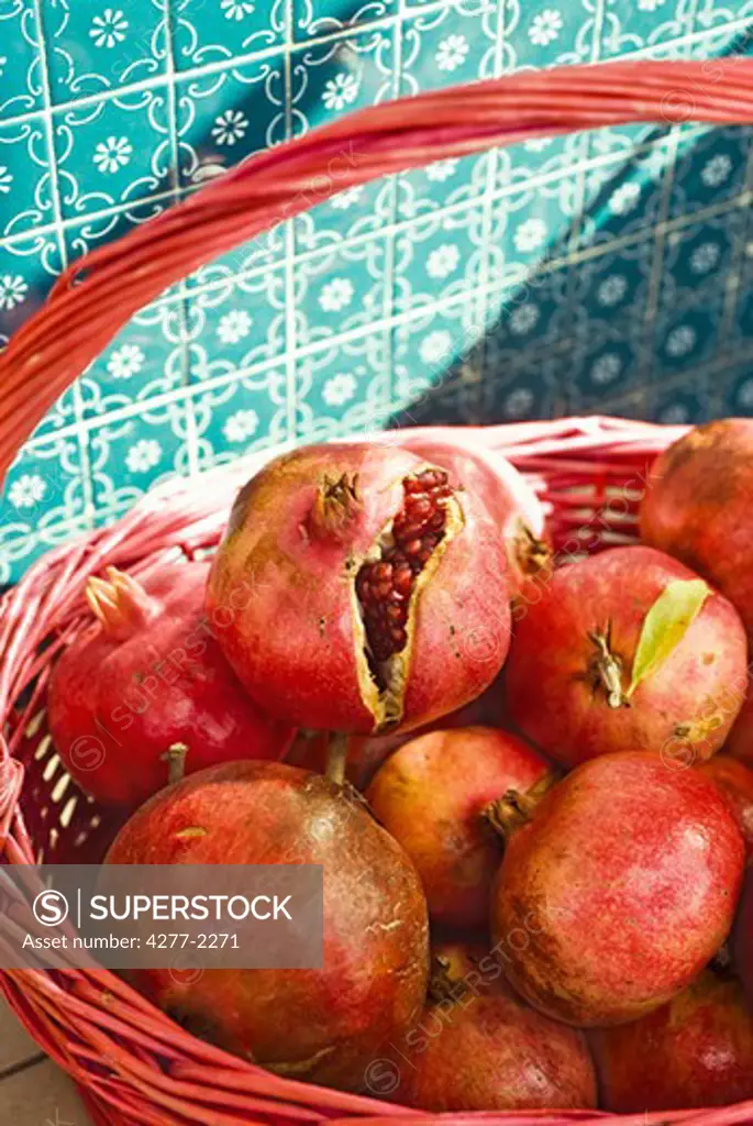 Ripe pomegranates in basket, one cracked open revealing seeds