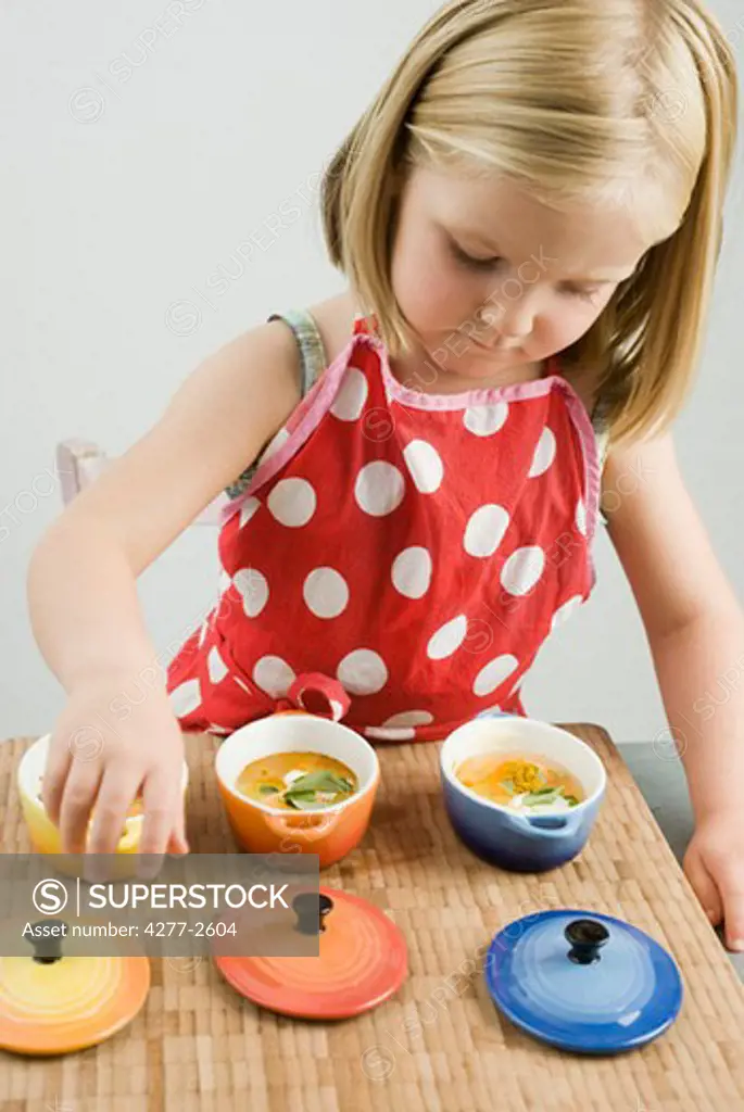 Little girl preparing baked eggs in small casserole dishes