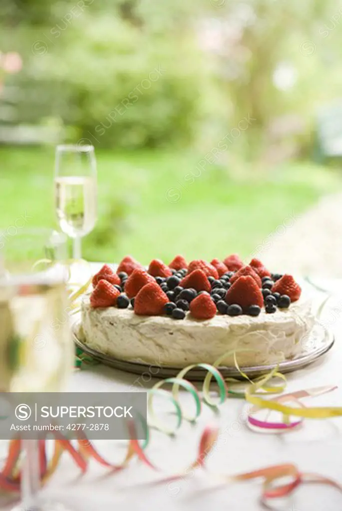 Strawberry blueberry cake and champagne on table decorated with party streamers