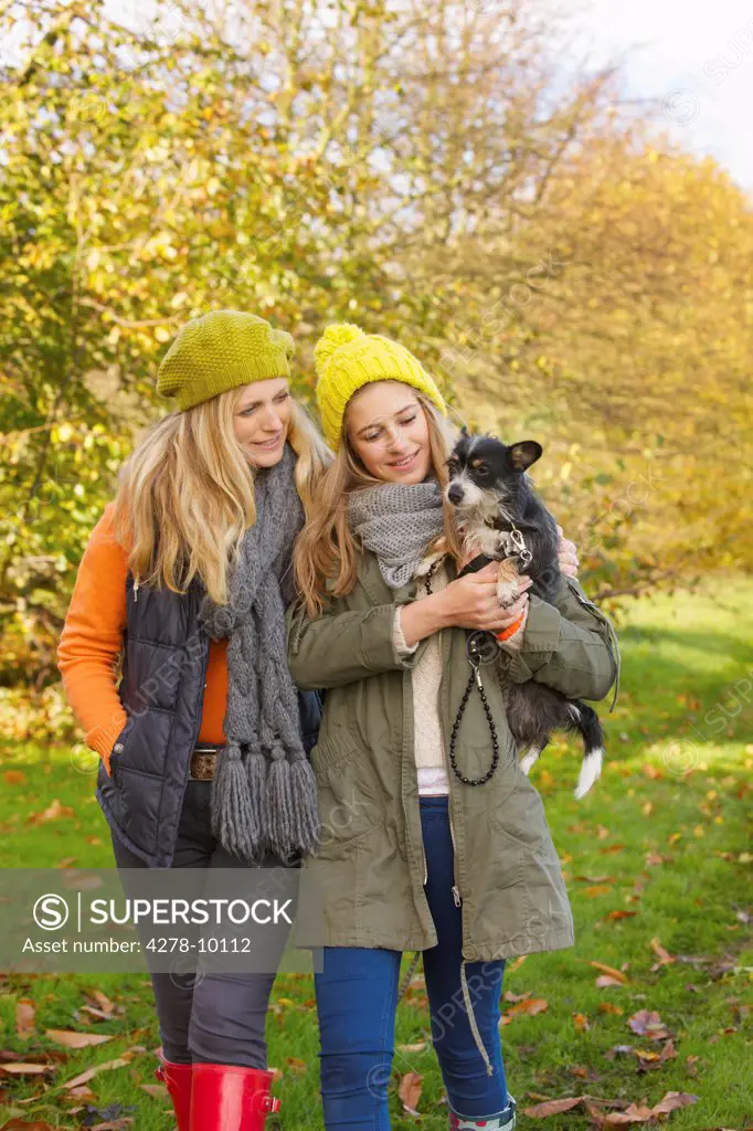 Mother and Daughter Walking in Park Carrying Dog