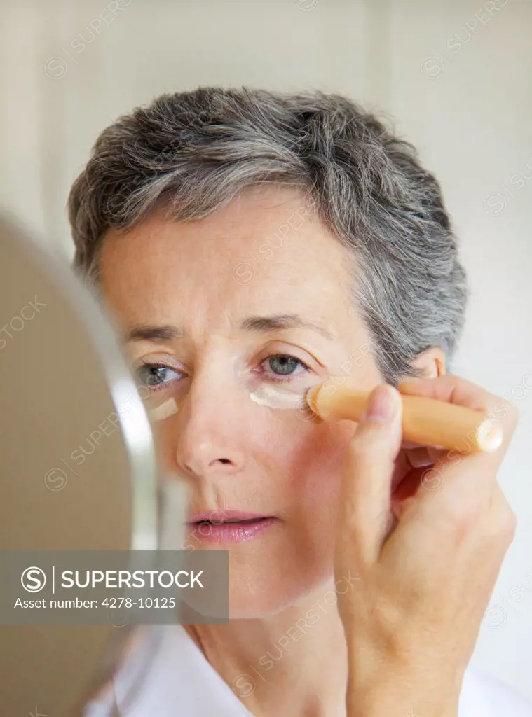 Woman Looking in Mirror Applying Concealer