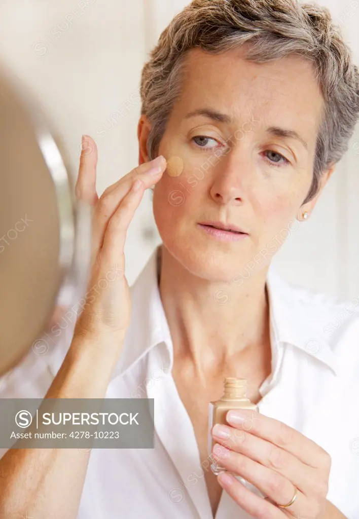 Woman Looking in Mirror Applying Foundation
