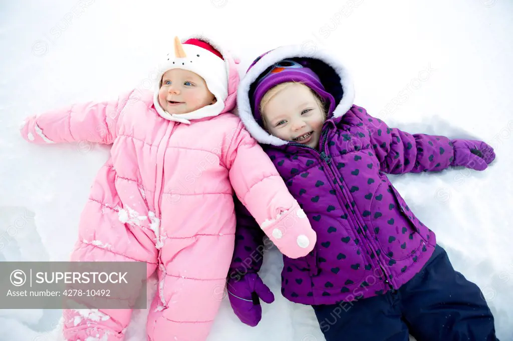 Girl with Baby Sister Lying Down in the Snow