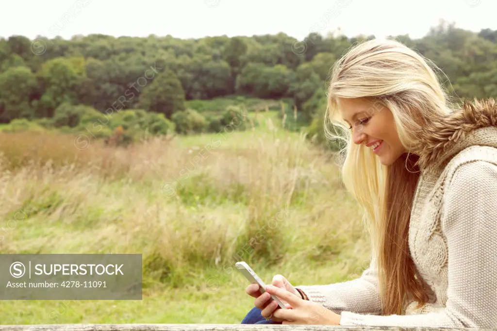 Young Woman in Field Using Smartphone