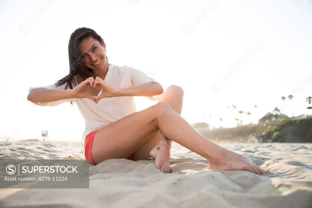 Woman Sitting on Sand Making Heart Shape with her Hands
