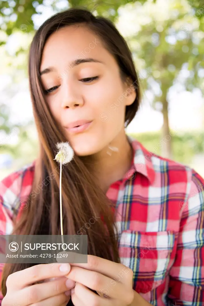 Young Woman Blowing Dandelion Seeds