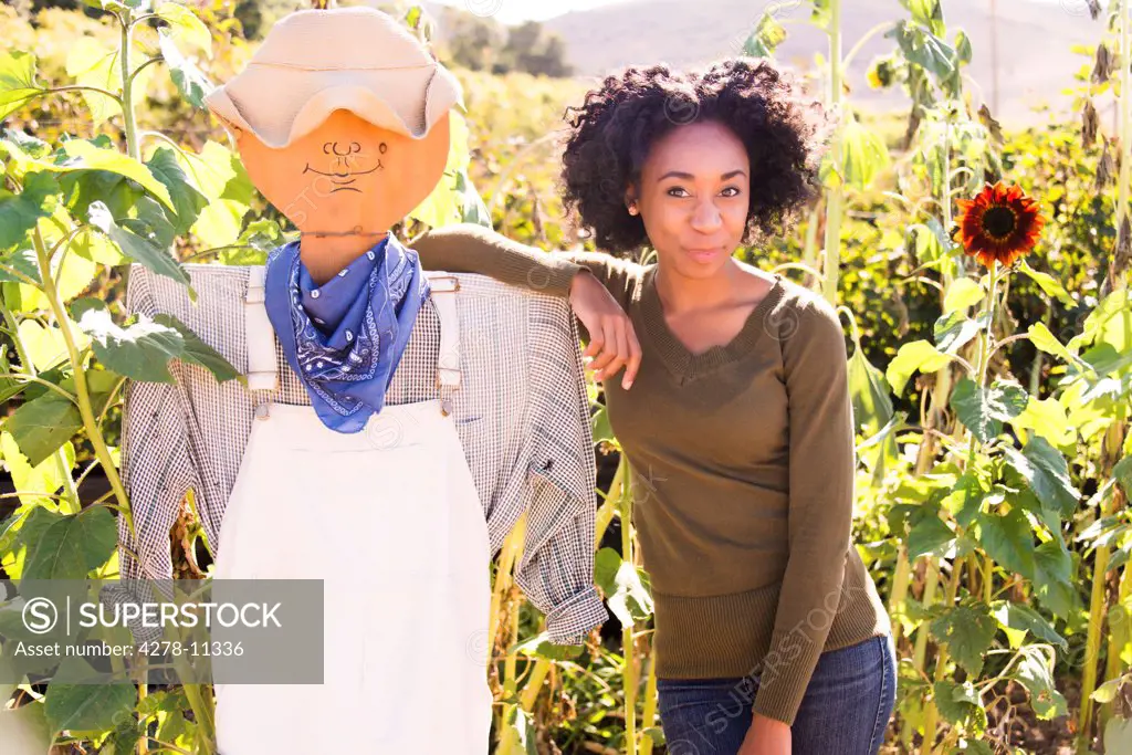 African American Woman in Sunflower Field Posing with Scarecrow