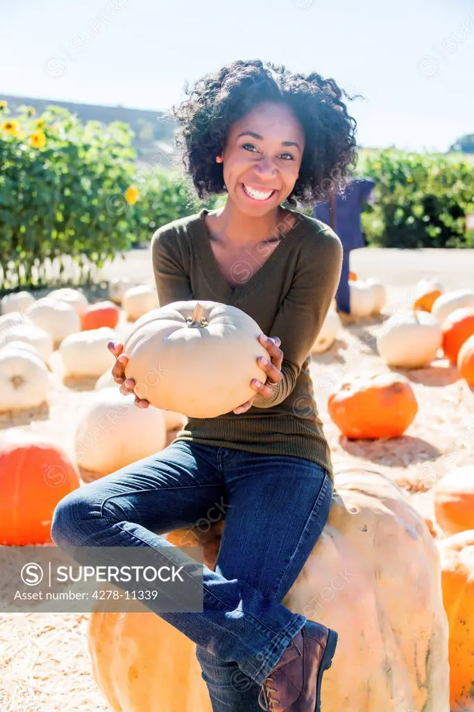 African American Woman Sitting on Pumpkin Smiling in a Pumpkin Patch