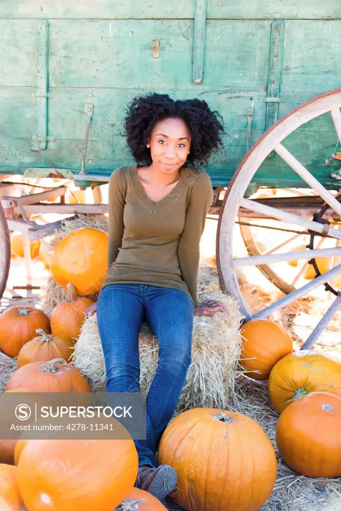 African American Woman Sitting on a Hay Bale Smiling in a Pumpkin Patch