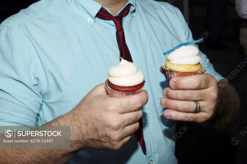 Man Holding Two Cupcakes with Whipped Cream, Cropped view