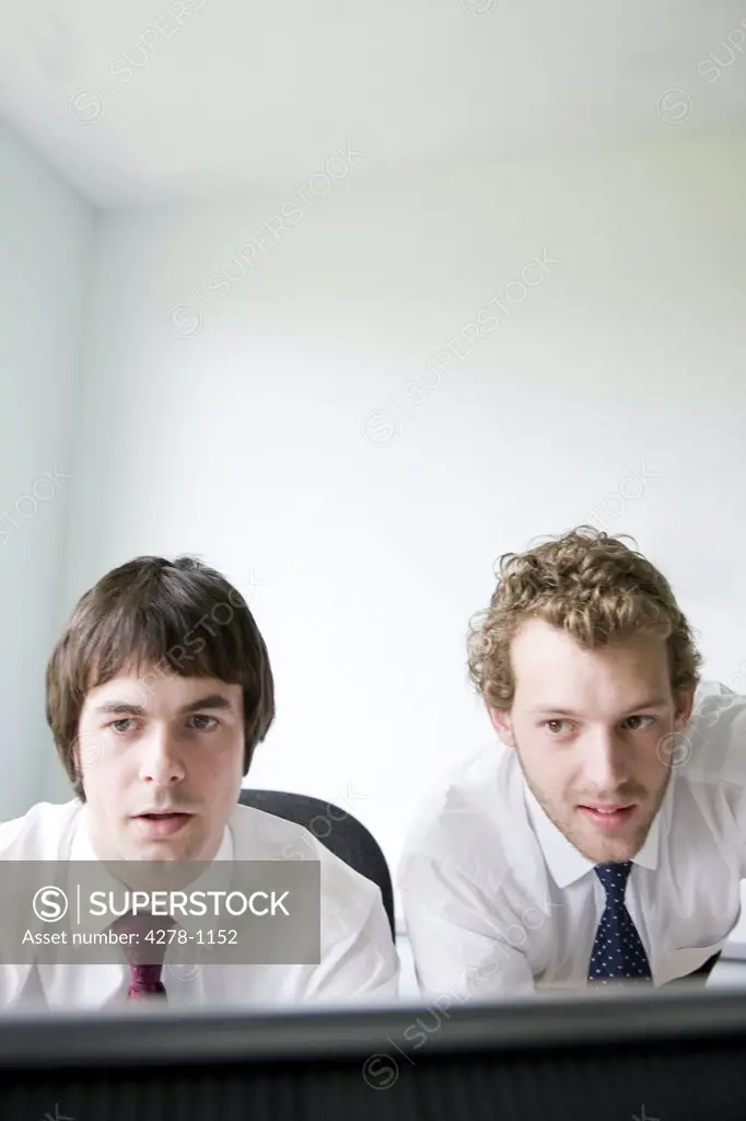 Portrait of two young businessmen looking at computer monitor