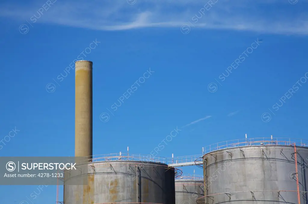 Storage tanks and industrial chimney against blue sky