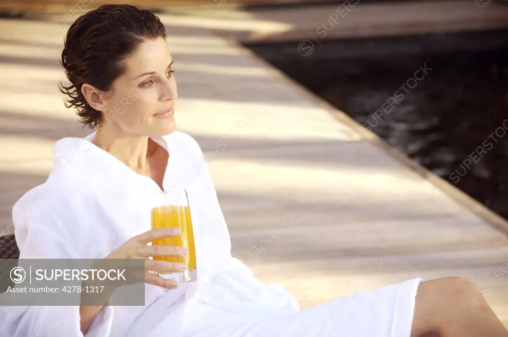 Woman sitting and drinking apple orange juice by swimming pool
