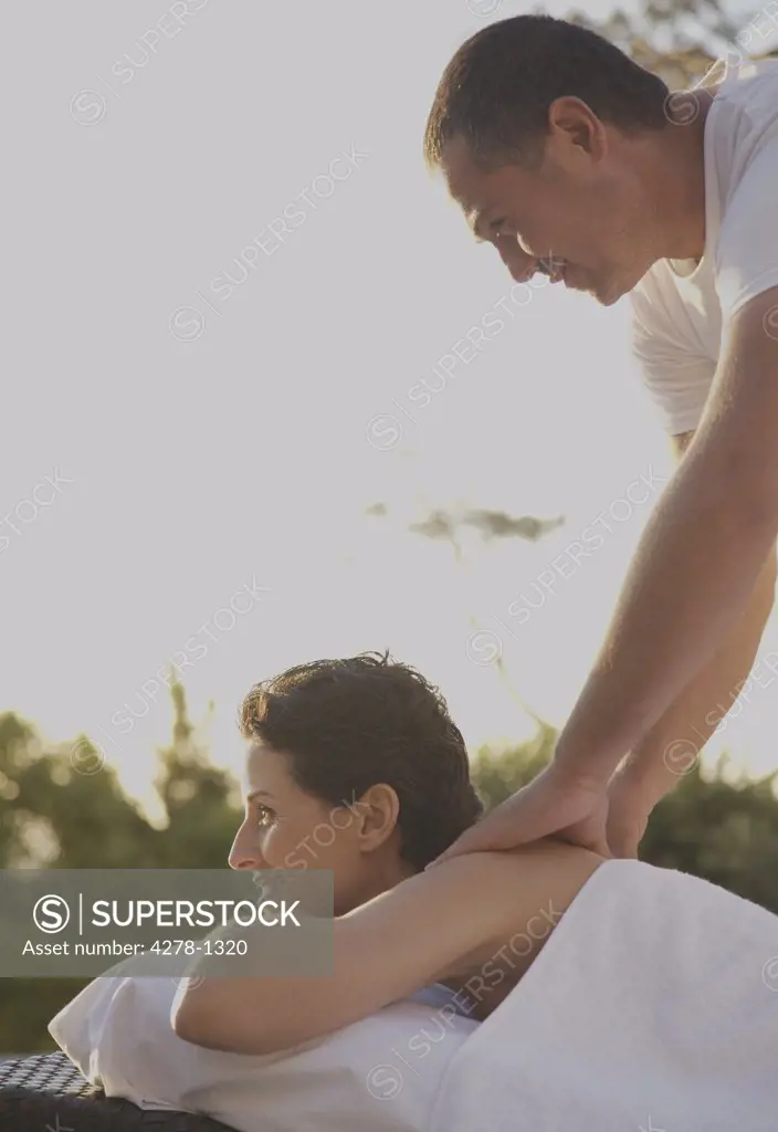 Massage therapist massaging woman on shoulders outdoors