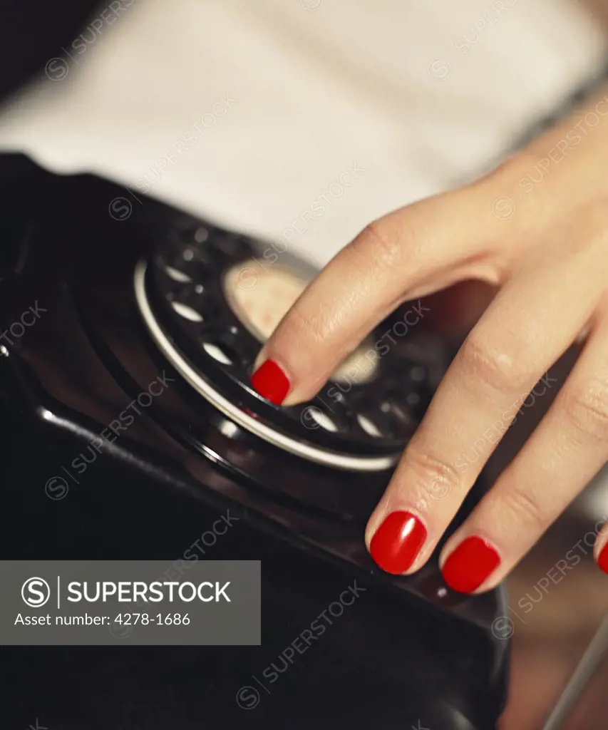 Close up of woman's hand with red nail varnish dialing on a black telephone