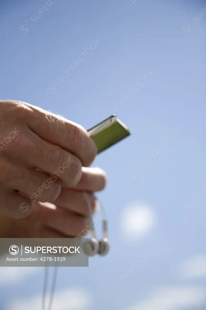 Extreme close up of hands and earphones against blue sky