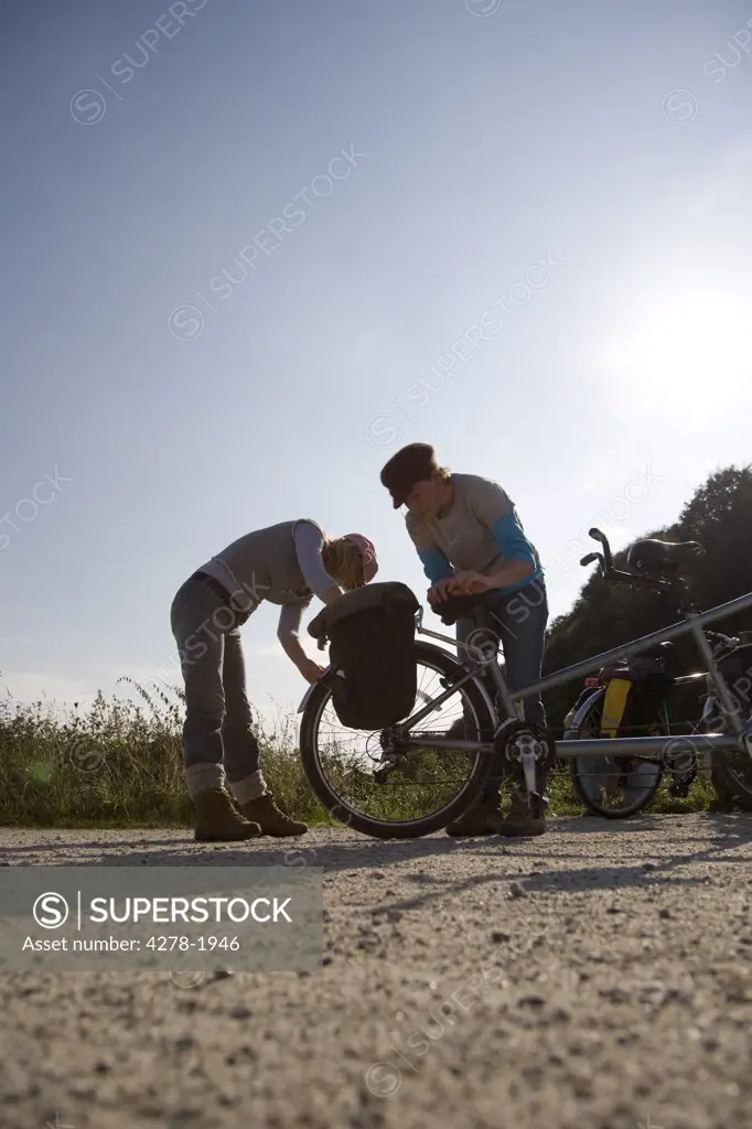 Two women checking tandem bicycle wheel in country road