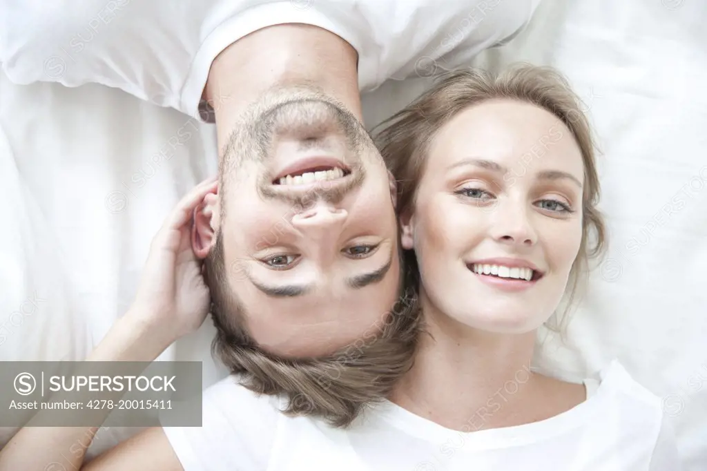 Smiling Couple Lying on Bed Facing Opposite Directions