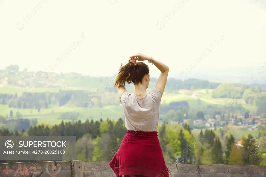 Back View of Young Woman Adjusting Hair Looking at Landscape
