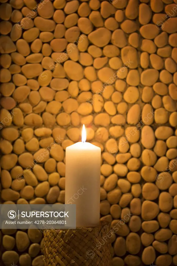Burning Candle against Pebble Tiles
