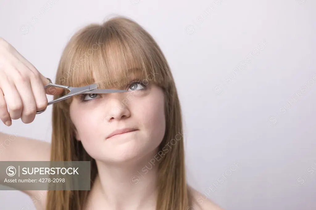 Young woman cutting own hair with scissors