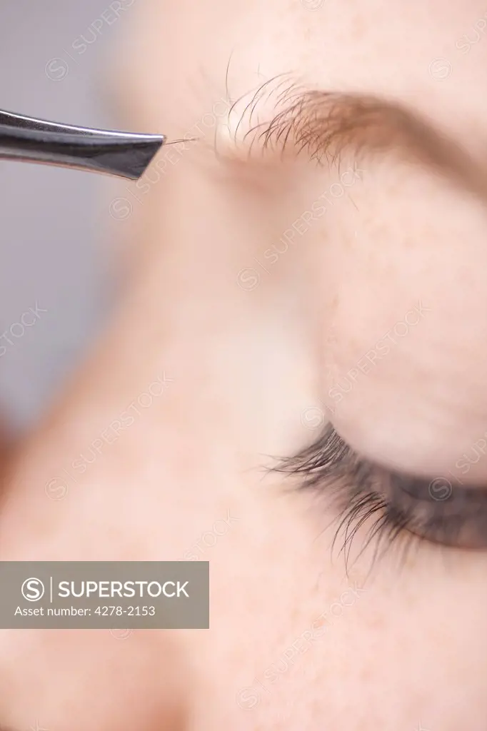 Extreme close up of young woman plucking own eyebrow hair with tweezers