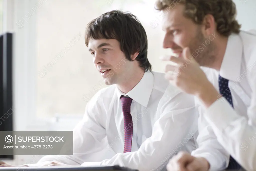Two young businessmen leaning on desk