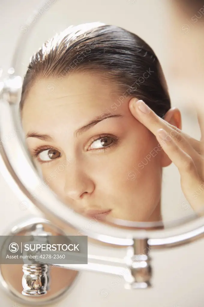 Close up of a young woman looking into round mirror checking her face