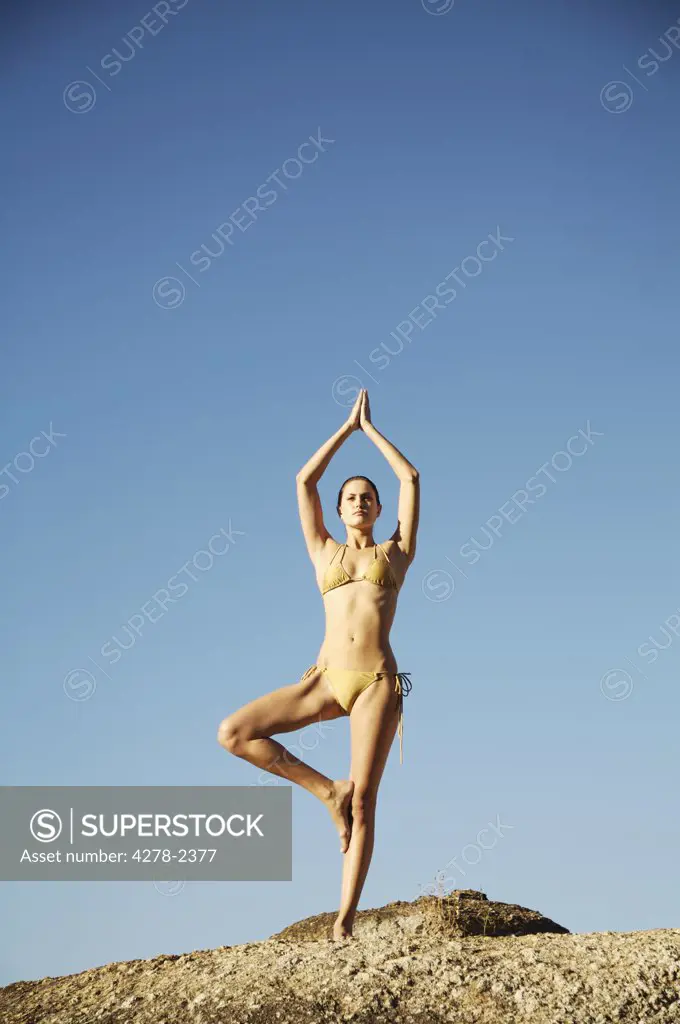 Portrait of a woman in the tree pose of yoga against blue sky