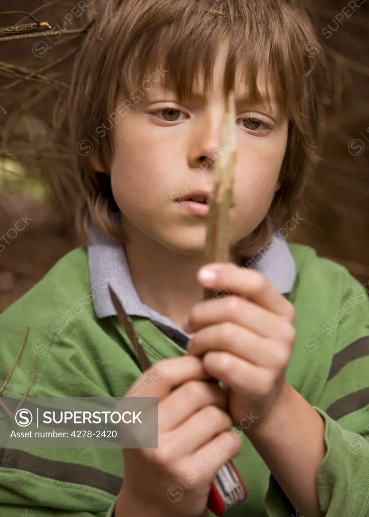 Close up of boy sharpening a wooden stick in a campsite