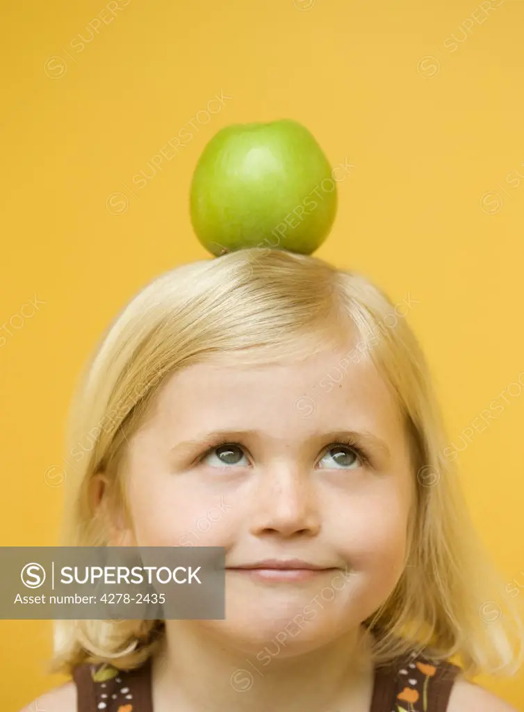 Girl with a green apple on top of her head looking up