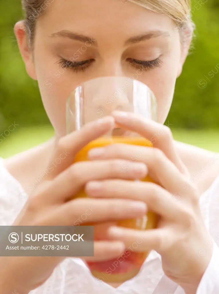 Close up of a young woman drinking and holding a glass of orange juice