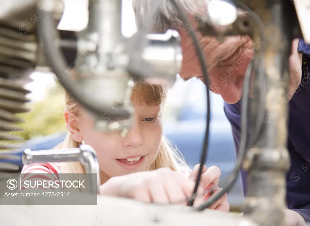 Young girl helping grandfather repairing motorbike engine