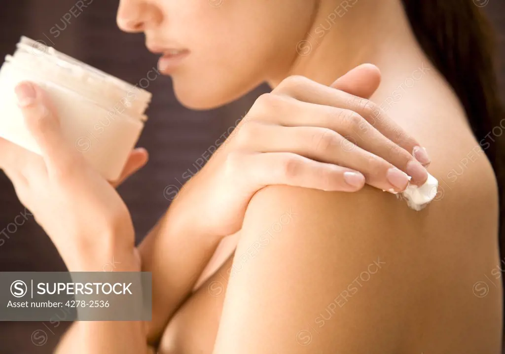 Close up of a young woman holding cream jar and  applying cream on shoulder