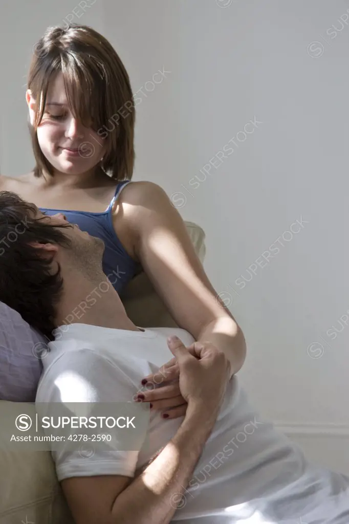 Young woman lying on sofa embracing man sitting on floor