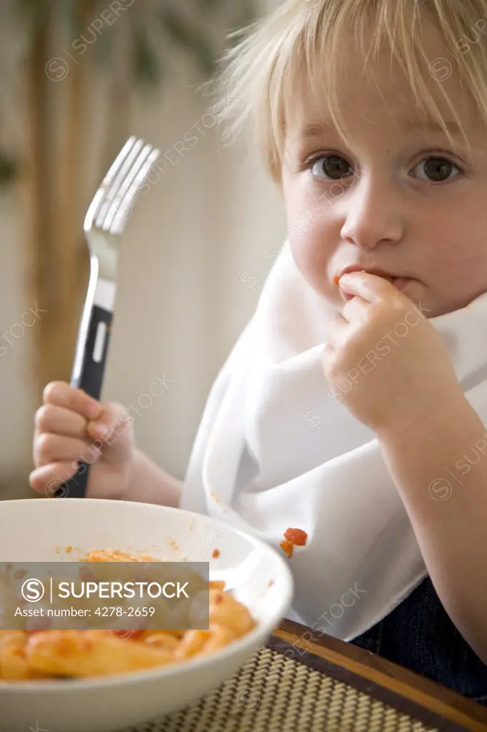 Portrait of young blonde boy eating pasta