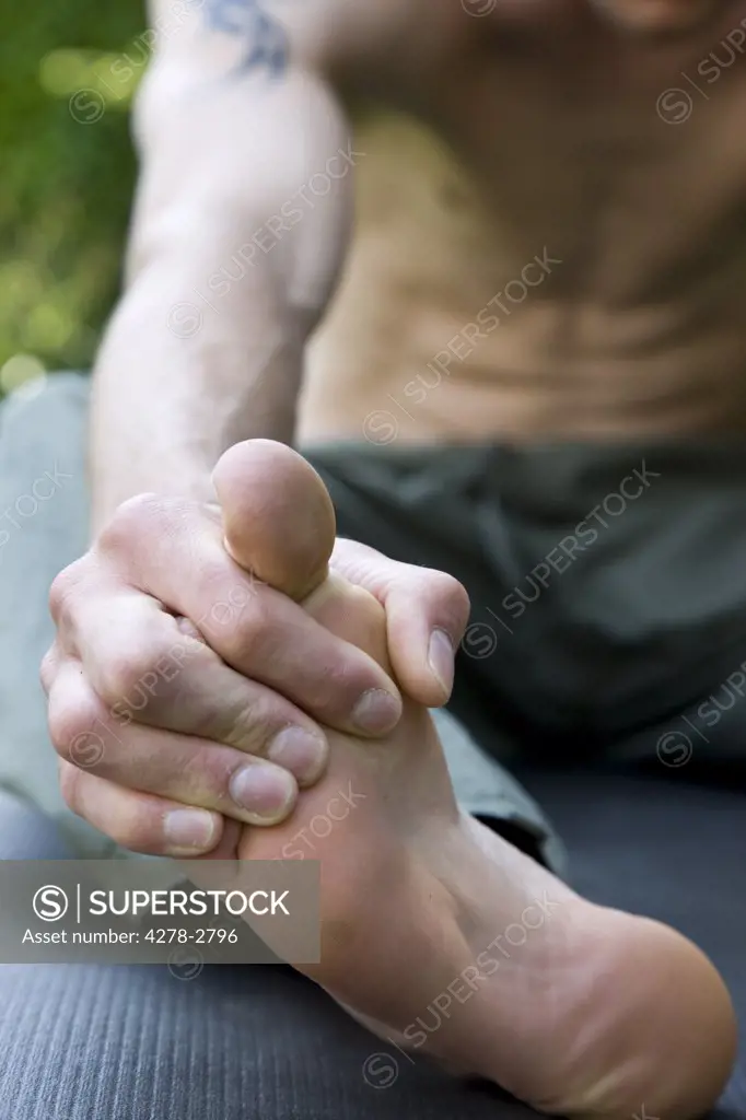 Close up of man body sitting on yoga mat holding foot