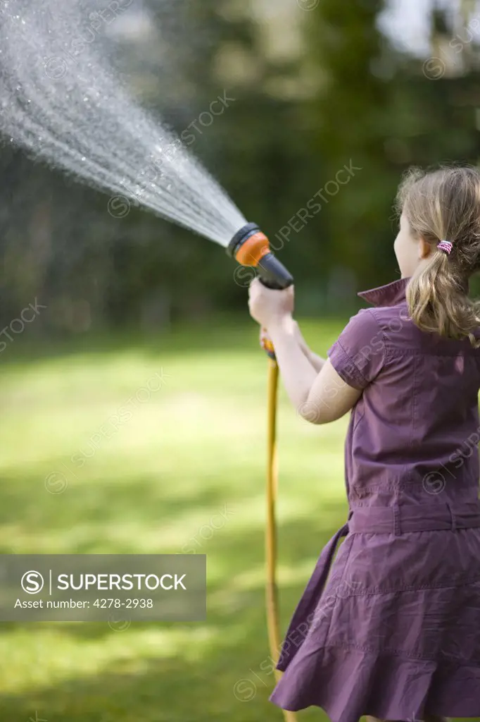 Back of young girl spraying the lawn with garden hose