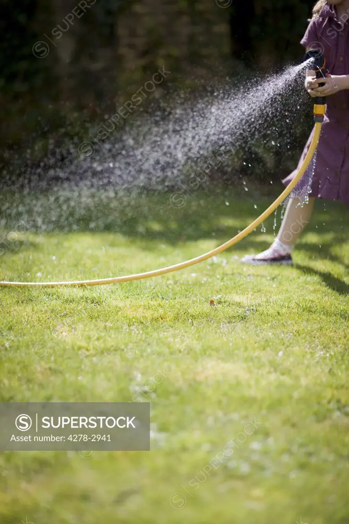 Headless young girl spraying the lawn with garden hose