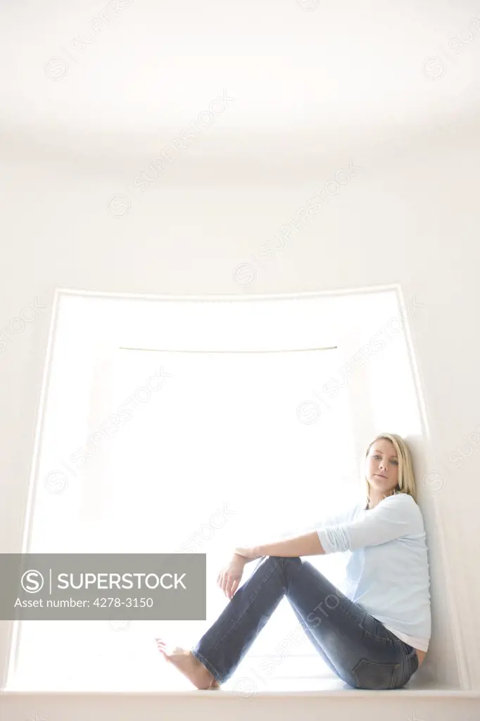 Young blonde woman sitting on a window sill