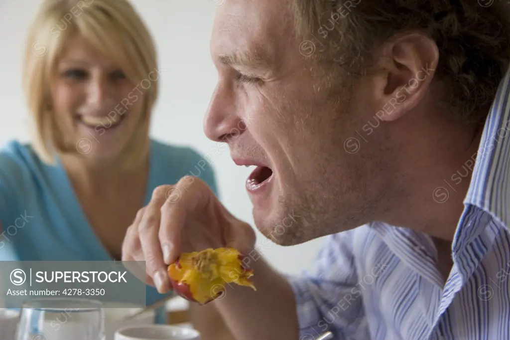 Couple having breakfast man laughing and eating peach