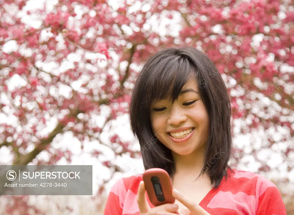 Smiling young teenaged girl holding and looking at cell phone