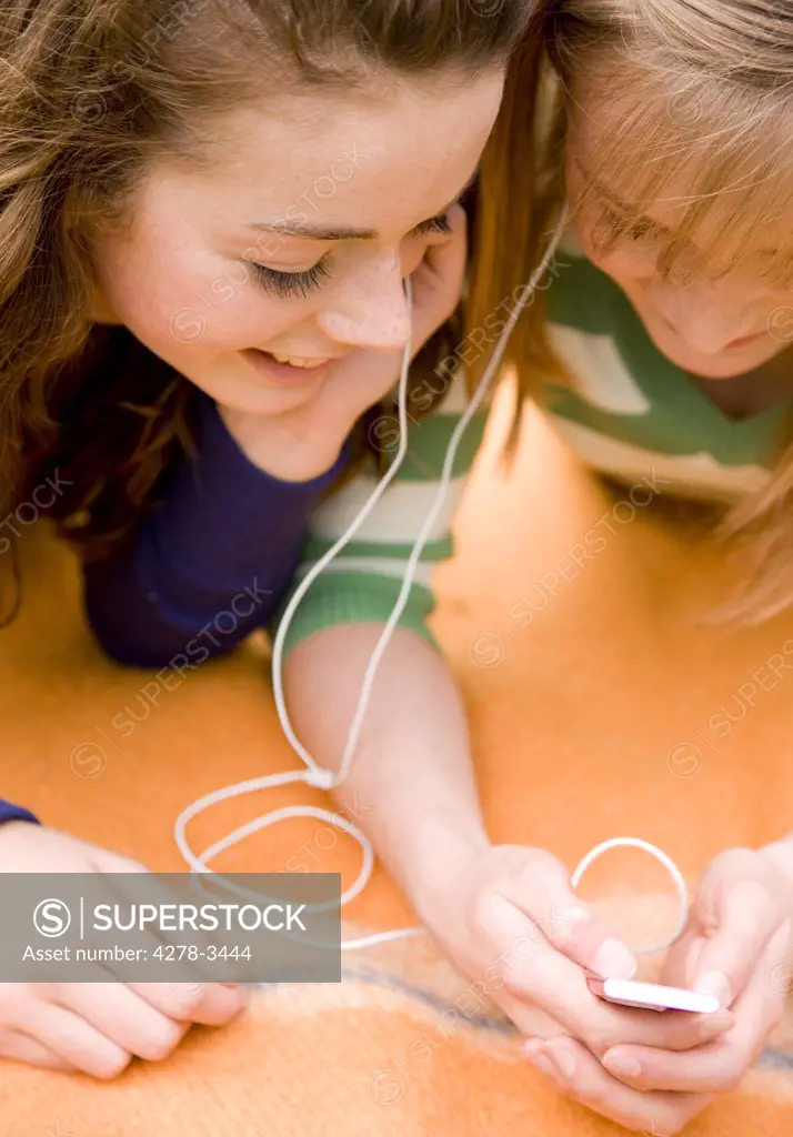 Two smiling teenaged girls lying on a blanket holding and mp3 player and listening to music