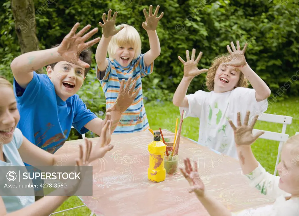 Children smiling and laughing with their arms up and hands covered in paint